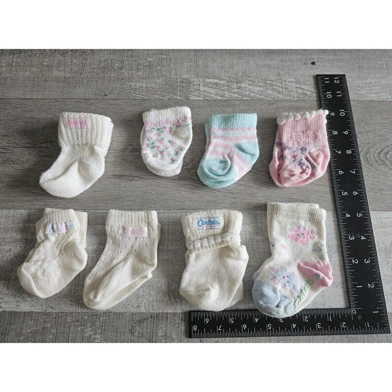 Puede incluir: Una colecci&oacute;n de ocho pares de calcetines para beb&eacute; en varios colores y patrones, incluyendo dise&ntilde;os blancos, rosas, azules y florales. Algunos calcetines tienen la palabra "Cartoks" impresa en ellos.