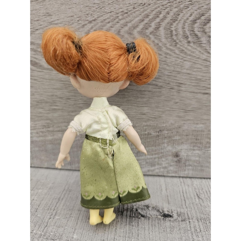 Puede incluir: Una mu&ntilde;eca peque&ntilde;a con el pelo rojo en coletas que lleva una camisa blanca y una falda verde con un dobladillo festoneado.