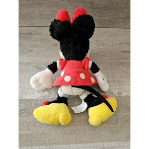 K&ouml;nnte beinhalten: Ein Pl&uuml;schtier von Minnie Mouse, die ein rotes Kleid mit wei&szlig;en Punkten und gelbe Schuhe tr&auml;gt. Sie hat schwarzes Fell und einen schwarzen Schwanz.