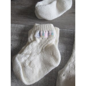 Puede incluir: Un par de calcetines blancos para beb&eacute; con una peque&ntilde;a etiqueta que dice "SHYTOSH" en letras de colores.