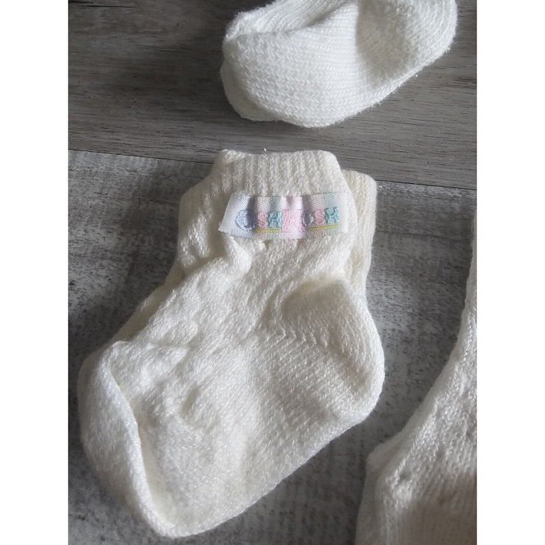 Puede incluir: Un par de calcetines blancos para beb&eacute; con una peque&ntilde;a etiqueta que dice "SHYTOSH" en letras de colores.