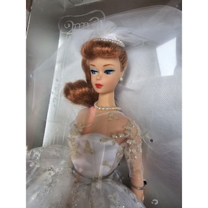 Peut inclure: Une poupée Barbie vintage vêtue d'une robe de mariée en dentelle blanche avec un voile et un collier de perles. La poupée a les cheveux roux et les yeux bleus.