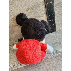 以下が含まれることがあります： 木製の表面に座っている、黒髪と耳を持つ赤いぬいぐるみのおもちゃです。
