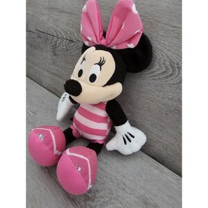 May include: Pink and black plush Minnie Mouse toy wearing a pink and white striped swimsuit. The toy has a pink bow with white polka dots and white gloves.