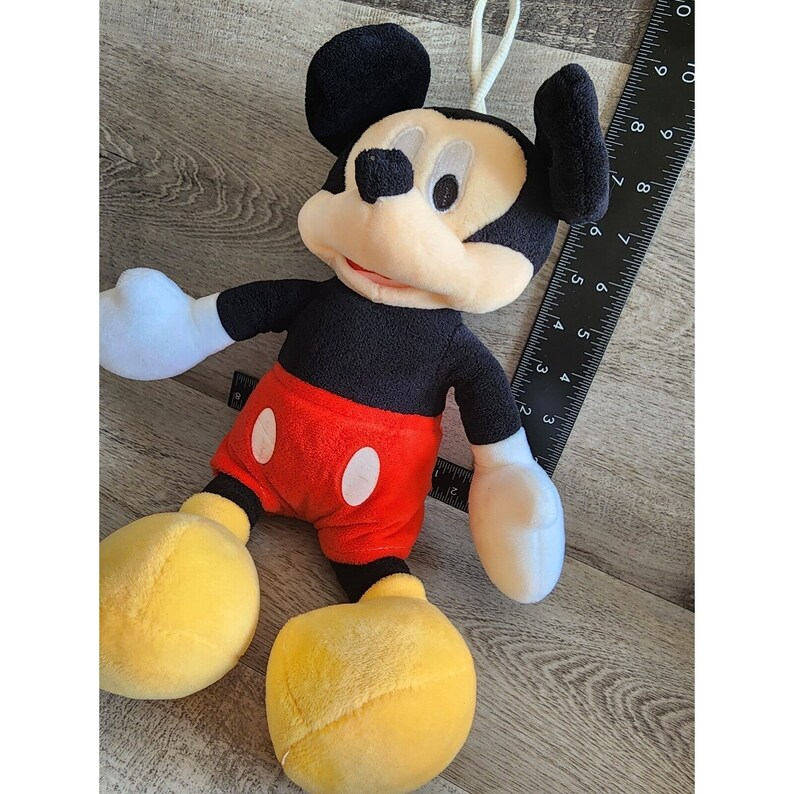 May include: A plush Mickey Mouse toy with black fur, red shorts, and yellow shoes. The toy has a white face with black eyes and a red nose.