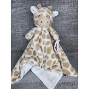 May include: A plush giraffe-themed baby security blanket. The blanket features a giraffe head with ears and a soft, tan and white spotted pattern. It has a white, plush backing and a loop for easy holding.