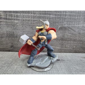 May include: A Thor action figure, featuring a white helmet with wings, blonde hair, and a red cape. The figure is in a dynamic pose, holding a gray hammer, and stands on a gray base. The figure is wearing a blue and gray outfit.