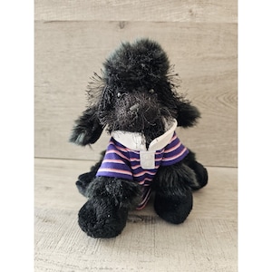 May include: Black plush poodle wearing a purple and pink striped shirt with a white collar.