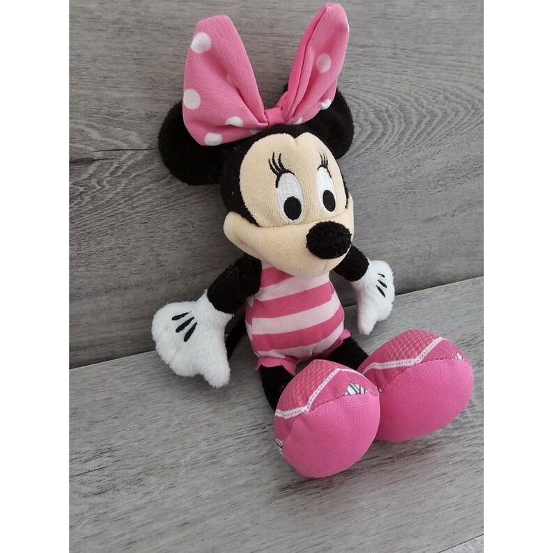 May include: Pink and black plush Minnie Mouse toy wearing a pink and white striped swimsuit. She has a pink bow with white polka dots on her head.