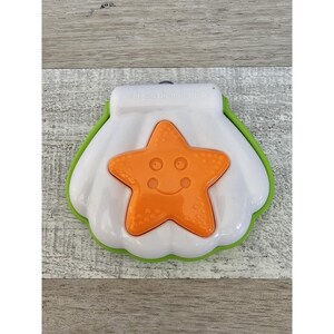 May include: A white seashell-shaped baby mobile with a green trim and an orange starfish with a smiling face in the center. The mobile has the text "Sweet sea dream mobile" printed on the top.