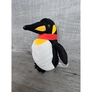 Könnte beinhalten: Schwarz-weißes Plüschtier-Pinguin mit rotem Schal. Der Pinguin hat gelbe Akzente um die Augen und den Schnabel.