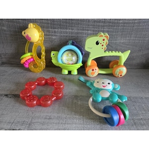 May include: A collection of colorful baby toys, including a yellow seahorse rattle, a green turtle with a spinning center, a green dinosaur on wheels, a red teething ring, and a blue monkey rattle with colorful rings.