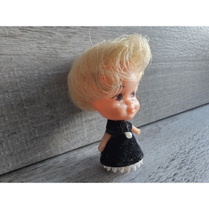 May include: A small plastic doll with blonde hair wearing a black dress with a white lace trim.