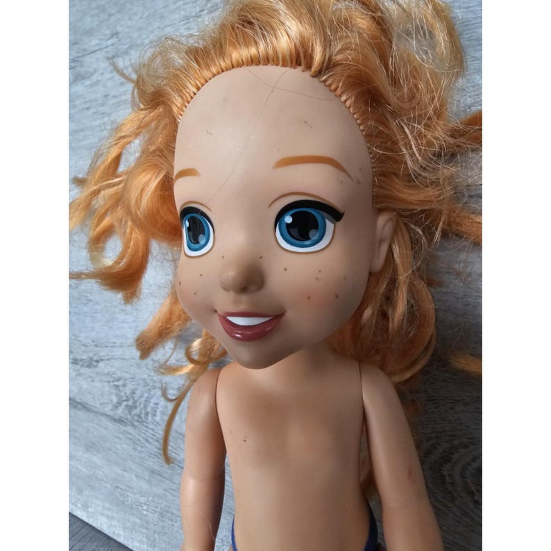 May include: A red-haired doll with blue eyes and freckles. The doll is wearing a blue swimsuit and has a bare torso.