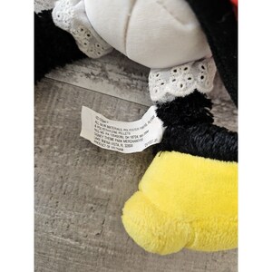 K&ouml;nnte beinhalten: Ein schwarzes und gelbes Pl&uuml;schtier mit einem wei&szlig;en Kragen und einer wei&szlig;en Spitzenborte. Das Spielzeug hat ein Etikett mit der Aufschrift "Disney, All New Materials, Polyester Fibres, Polythylene Pellets, Reg. No. PA 125400, OH 18724, MB 3000, Disney Theme Park Merchandise, Lake Buena Vista, FL 32830, Product of Vietnam, DVT027JH".