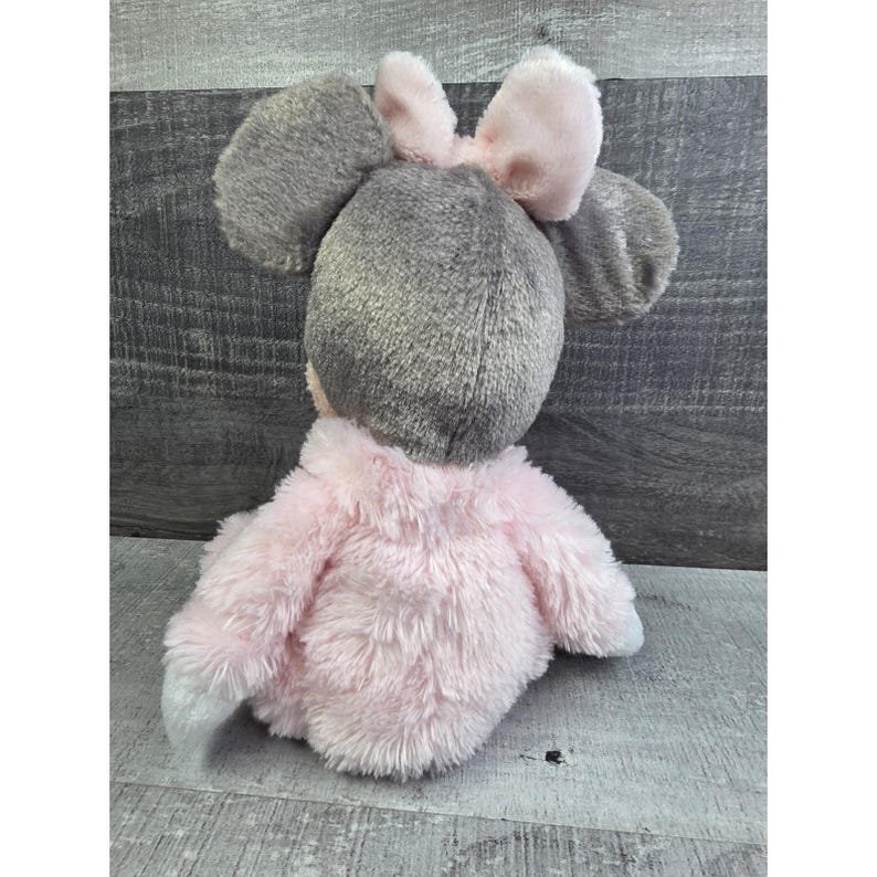 Puede incluir: Un peluche con forma de rat&oacute;n, visto desde atr&aacute;s. El rat&oacute;n tiene grandes orejas grises y un lazo rosa en la cabeza. El cuerpo est&aacute; cubierto de suave pelaje rosa, con patas blancas.