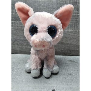 May include: A plush pig toy in shades of pink with large, sparkly blue eyes. The pig has large ears, a small snout, and silver glittery hooves. The toy is sitting upright, showcasing its soft, fluffy texture.
