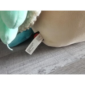 May include: A plush toy with a light blue, green, and white design. The toy has a tag that reads "Made in China, All New Material, 100% Polyester, Surface Washable, Do Not Bleach, Do Not Iron, Do Not Dry Clean, Do Not Tumble Dry."