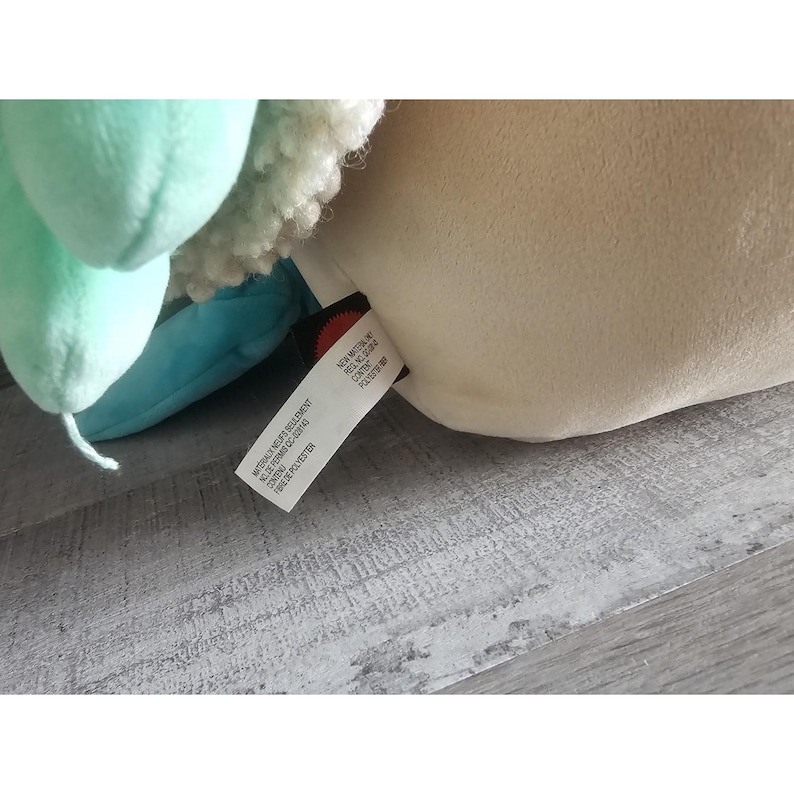 May include: A plush toy with a light blue, green, and white design. The toy has a tag that reads "Made in China, All New Material, 100% Polyester, Surface Washable, Do Not Bleach, Do Not Iron, Do Not Dry Clean, Do Not Tumble Dry."