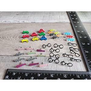 May include: Assortment of colorful car and tie push pins. The cars are red, yellow, blue, green, and black. The ties are pink, blue, yellow, black and white, and red and blue.