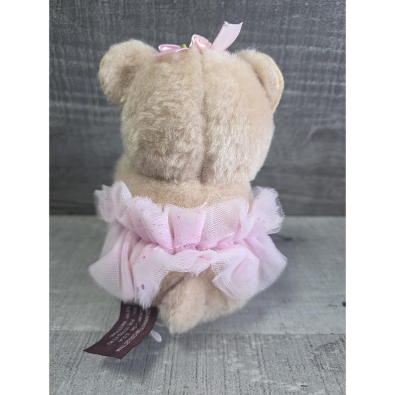Pu&ograve; includere: Un orsacchiotto beige con un tut&ugrave; rosa e un fiocco rosa. Il tut&ugrave; &egrave; fatto di strati di tulle rosa con un design scintillante. L'orso ha un piccolo fiocco rosa sulla testa. Un'etichetta marrone &egrave; attaccata all'orso.