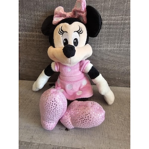 May include: A pink and black plush toy of Minnie Mouse wearing a pink dress with white polka dots and a sparkly pink bow.