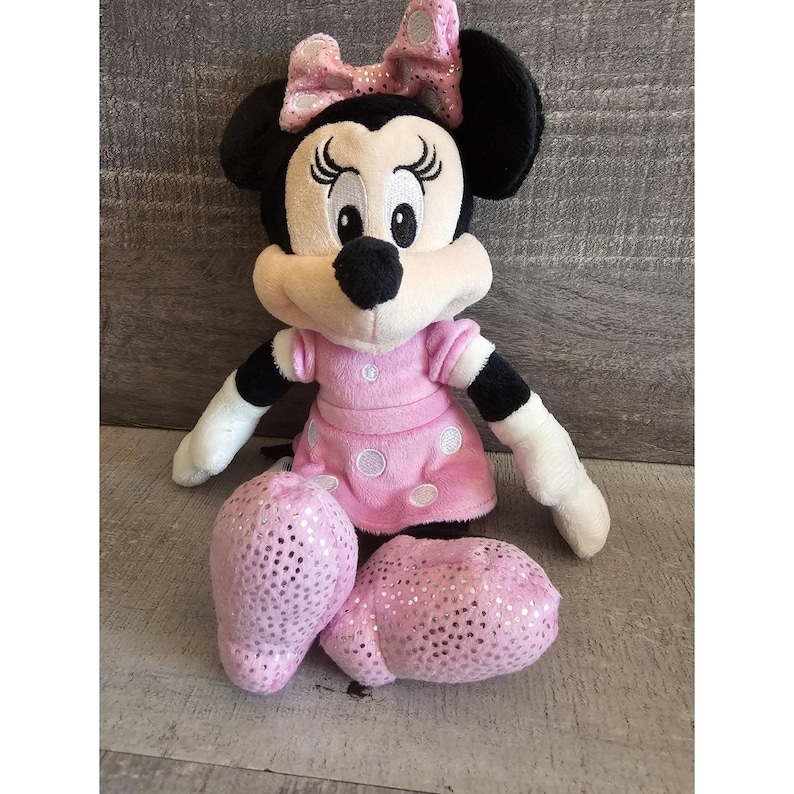 May include: A pink and black plush toy of Minnie Mouse wearing a pink dress with white polka dots and a sparkly pink bow.