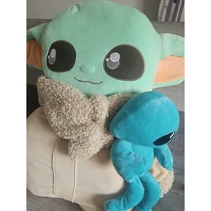 May include: A large green plush toy with a brown fur scarf and a smaller blue plush toy with large eyes.