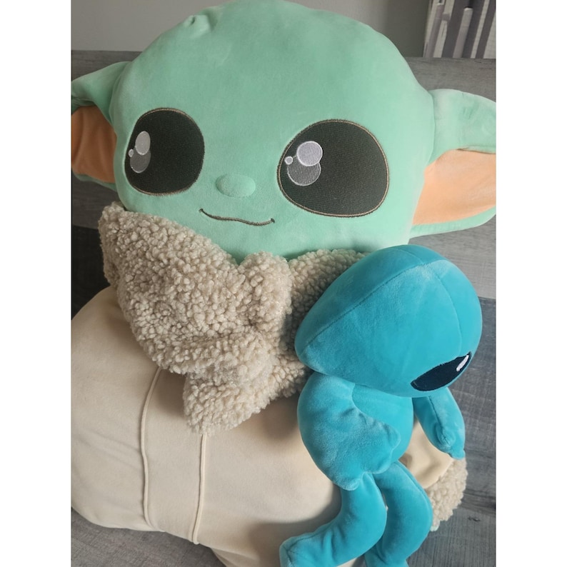 May include: A large green plush toy with a brown fur scarf and a smaller blue plush toy with large eyes.
