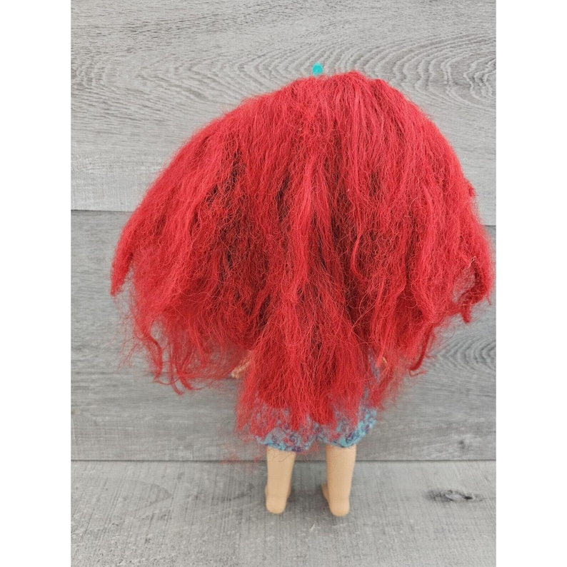 Puede incluir: Una mu&ntilde;eca con el pelo rojo largo y suelto, que lleva un vestido con estampado azul y blanco.