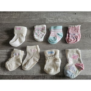 Puede incluir: Una colecci&oacute;n de ocho calcetines para beb&eacute; en varios colores y patrones, incluyendo blanco, rosa, azul y dise&ntilde;os florales. Algunos calcetines llevan el nombre de la marca "Carter's".