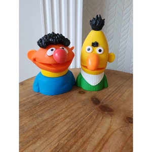 Könnte beinhalten: Zwei Figuren von Sesamstraße-Charakteren, eine ist ein gelber Big Bird mit einem langen orangefarbenen Schnabel und die andere ist ein brauner und orangefarbener Cookie Monster mit einem blauen Hemd.