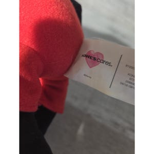 Puede incluir: Primer plano de un juguete de peluche rojo con detalles en negro. Se ve una etiqueta con el texto "KOHL'S cares" con un coraz&oacute;n y el logotipo de Disney. La etiqueta tambi&eacute;n incluye informaci&oacute;n del producto.
