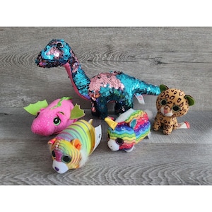 May include: A collection of five plush toys, including a pink dragon, a rainbow unicorn, a multi-colored striped tiger, a brown and black leopard, and a blue and pink sequined dinosaur.