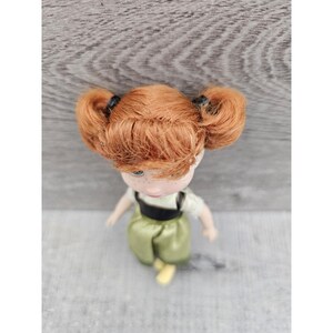 Puede incluir: Una mu&ntilde;eca peque&ntilde;a con el pelo rojo en coletas que lleva un vestido verde con un corpi&ntilde;o negro.