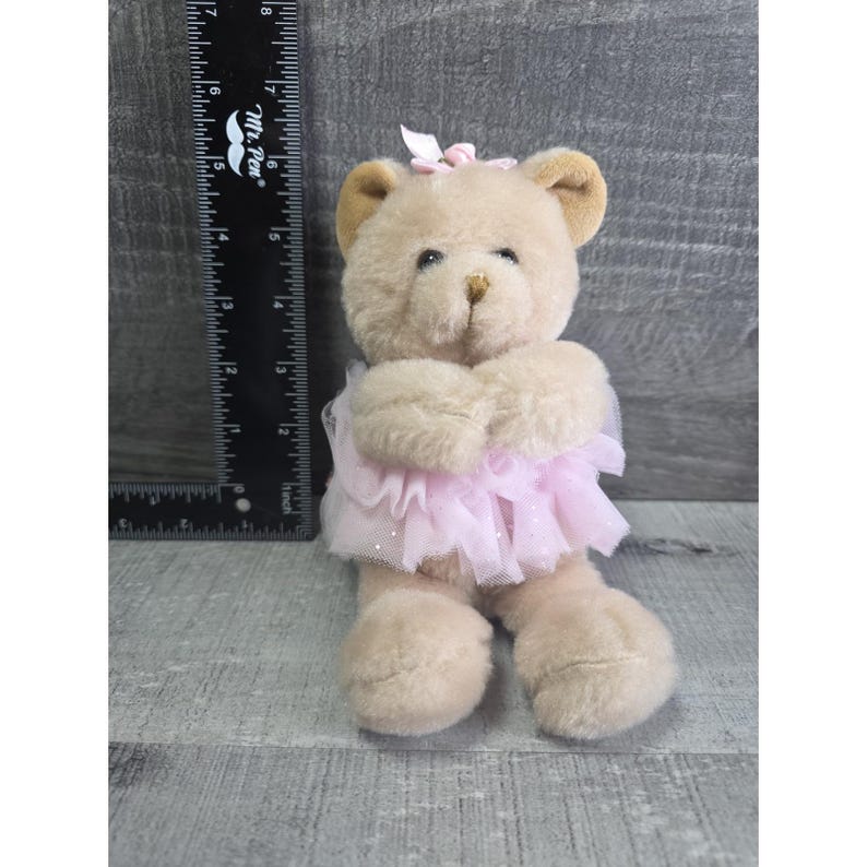 Pu&ograve; includere: Un orsacchiotto marrone chiaro con un tut&ugrave; rosa e un fiocco rosa. Il peluche ha orecchie marroni chiare e un naso marrone. Il tut&ugrave; &egrave; fatto di strati di tulle rosa. L'orso &egrave; alto circa 15 cm.