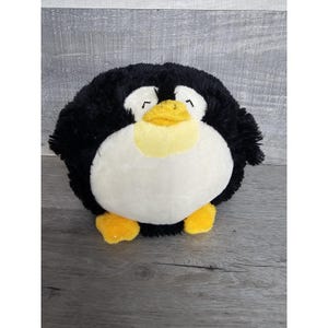 Puede incluir: Un peluche de pingüino con un cuerpo redondo. El pingüino tiene pelaje negro, vientre blanco, pico amarillo y pies amarillos. El juguete está diseñado para parecerse a un pingüino de dibujos animados.