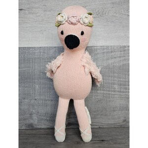 May include: Pink knitted flamingo doll wearing a flower crown and ballet shoes.