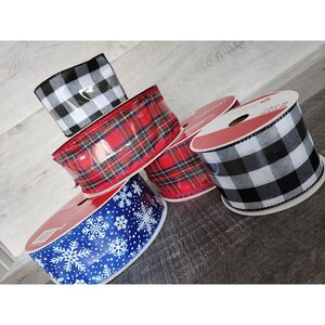 May include: Four rolls of ribbon in various patterns. The rolls are black and white checkered, red and black plaid, blue with white snowflakes, and red and black plaid.