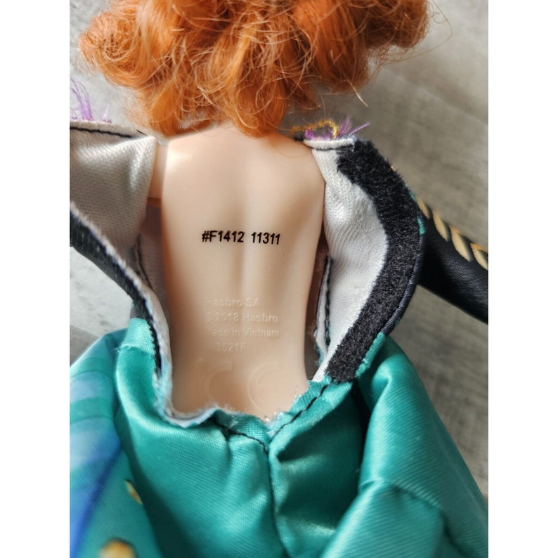 May include: A doll with red hair wearing a green and black dress. The doll's back has a label with the text "#F1412 11311".