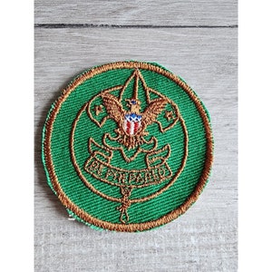 May include: A green and gold embroidered Boy Scout patch featuring the Boy Scout emblem and the words "Be Prepared".