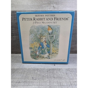 Puede incluir: Una caja azul con Peter Rabbit y sus amigos de Beatrix Potter. La caja tiene una ilustración de Peter Rabbit con un pájaro y una pala. El texto en la caja dice "Juego de 3 piezas de melamina".