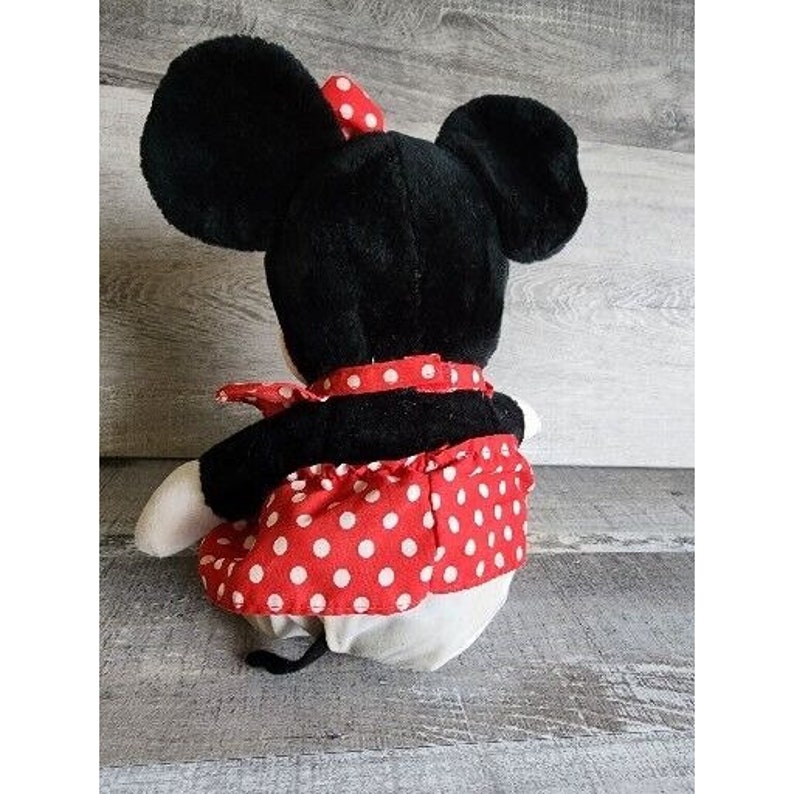 Peut inclure: Un jouet en peluche noir et blanc repr&eacute;sentant une souris de dessin anim&eacute; portant une robe &agrave; pois rouges et blancs. La souris a de grandes oreilles et un n&oelig;ud rouge.