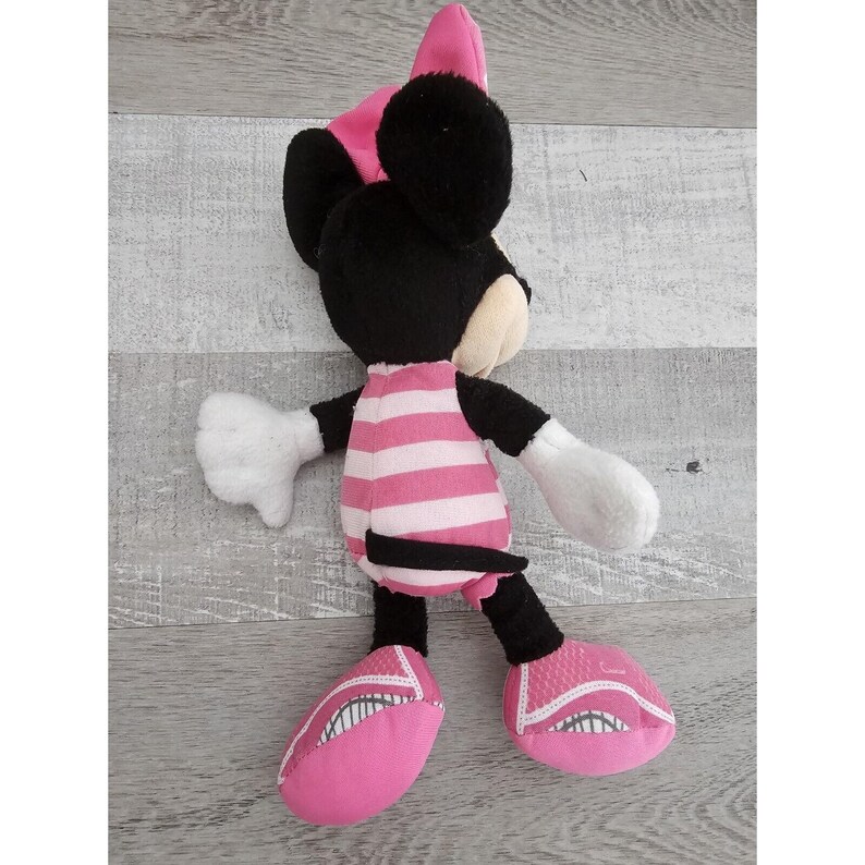May include: Pink and black plush toy of a cartoon mouse wearing a pink hat and a pink and white striped shirt. The toy has large black ears and pink shoes.