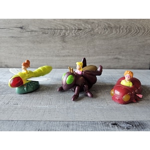 May include: Three plastic toy vehicles featuring characters from the movie A Bug's Life. The vehicles are a green and yellow dragonfly, a brown beetle, and a red ladybug.