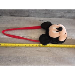 May include: A Mickey Mouse headband with a plush face and black ears. The headband is red and measures approximately 22 inches in length. The Mickey Mouse face is tan, black, and white.