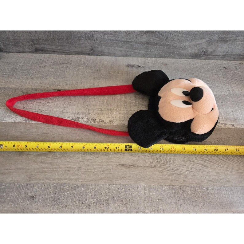 May include: A Mickey Mouse headband with a plush face and black ears. The headband is red and measures approximately 22 inches in length. The Mickey Mouse face is tan, black, and white.