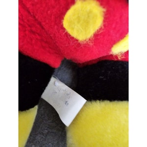 May include: Close-up of a red, black and yellow plush toy with a white tag that says "Made in China".