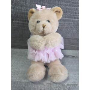 Pu&ograve; includere: Un orsacchiotto di peluche seduto, con un tut&ugrave; rosa e un fiocco abbinato. L'orso ha una pelliccia marrone chiaro con orecchie marroni pi&ugrave; scure e un naso dorato. Il tut&ugrave; &egrave; realizzato in un tessuto rosa trasparente con glitter.