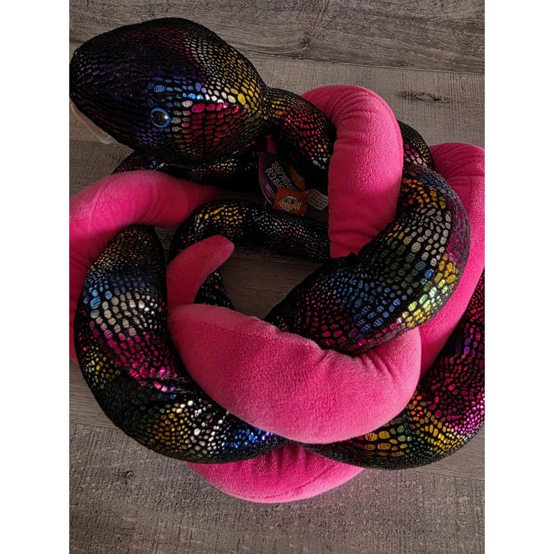 Op de afbeelding: Een pluche slangenknuffel met een zwarte, iriserende body en felroze accenten. De slang is opgerold, met een gedetailleerd schubbenpatroon en een vriendelijke uitdrukking. Een label is bevestigd.